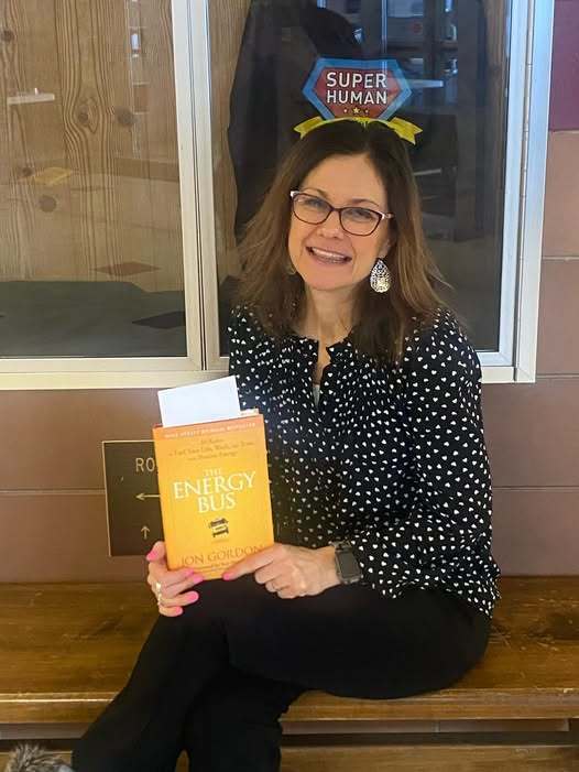 Women in a black and white polka dot shirt holding a yellow book while sitting.