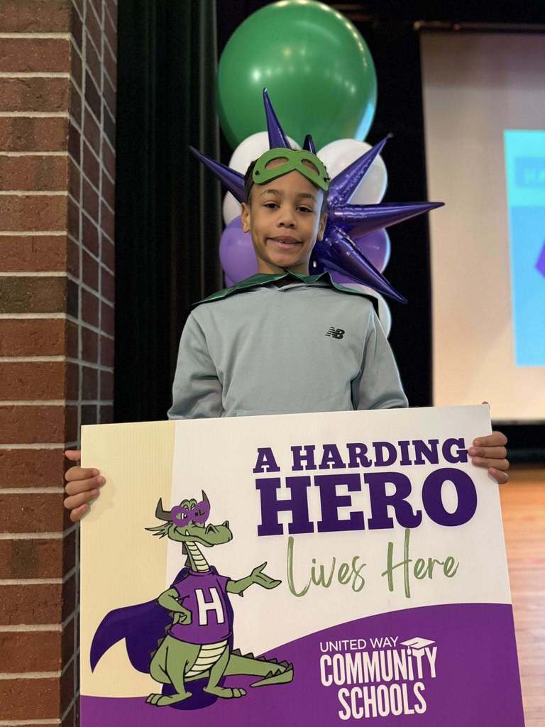 Young boy in a light blue top holding a "Harding Hero" Sign. 