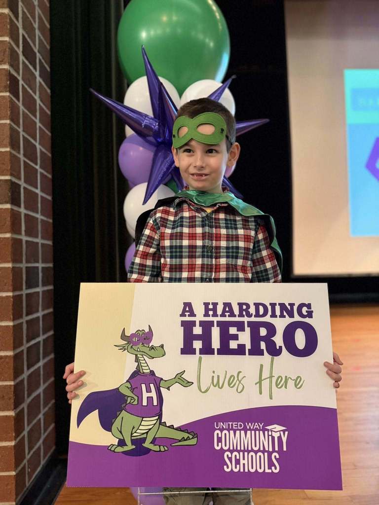 A boy in a plaid shirt and is holding a "Harding Hero" Sign. 