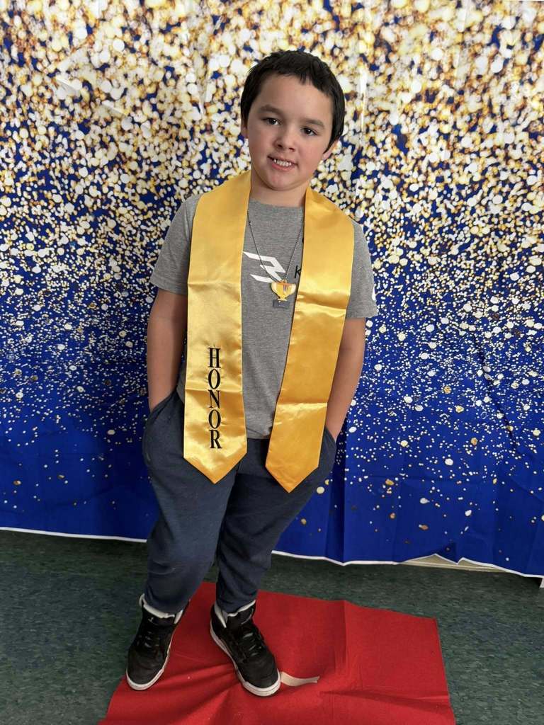 Young boy wearing a gray top and a gold honors stole.