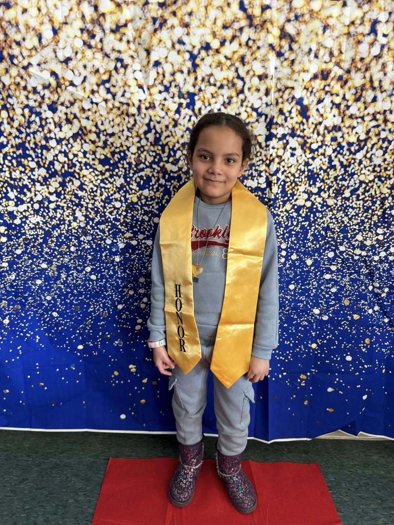 Young child wearing a gray top and a gold honors stole.
