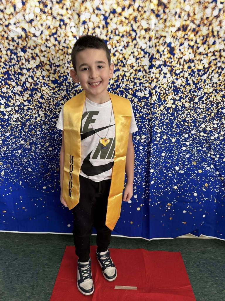 Young boy wearing a white shirt and a gold honors stole.