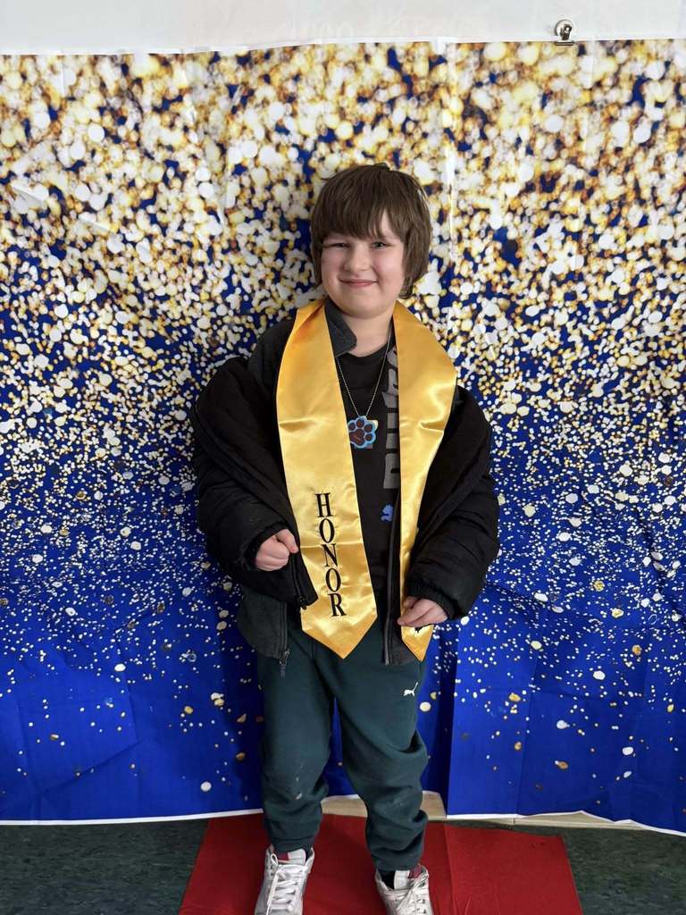 A young kid wearing a black top and a gold honors stole.