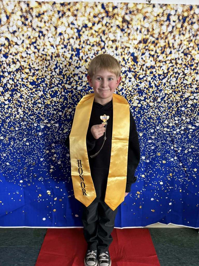 Young boy wearing a black shirt and a gold honors stole.