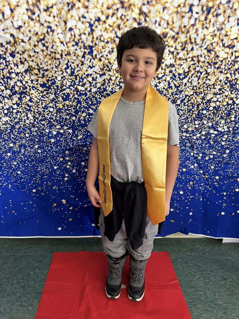 Young boy wearing a gray top and a gold honors stole.