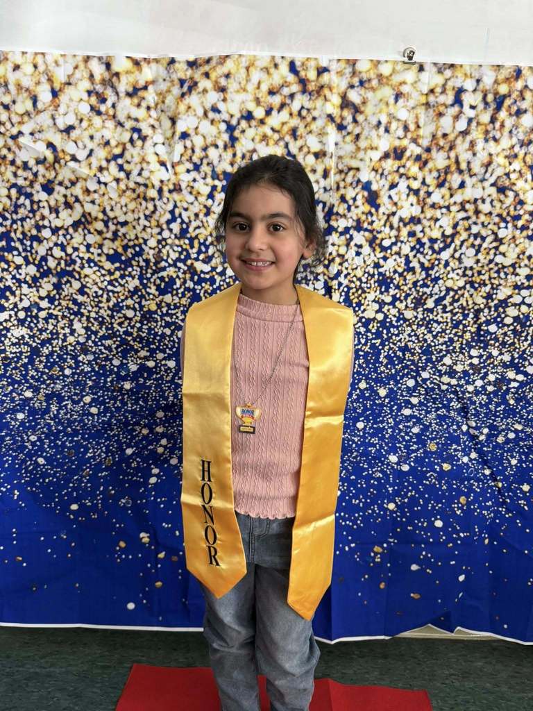 Young girl wearing a pink shirt and a gold honors stole.