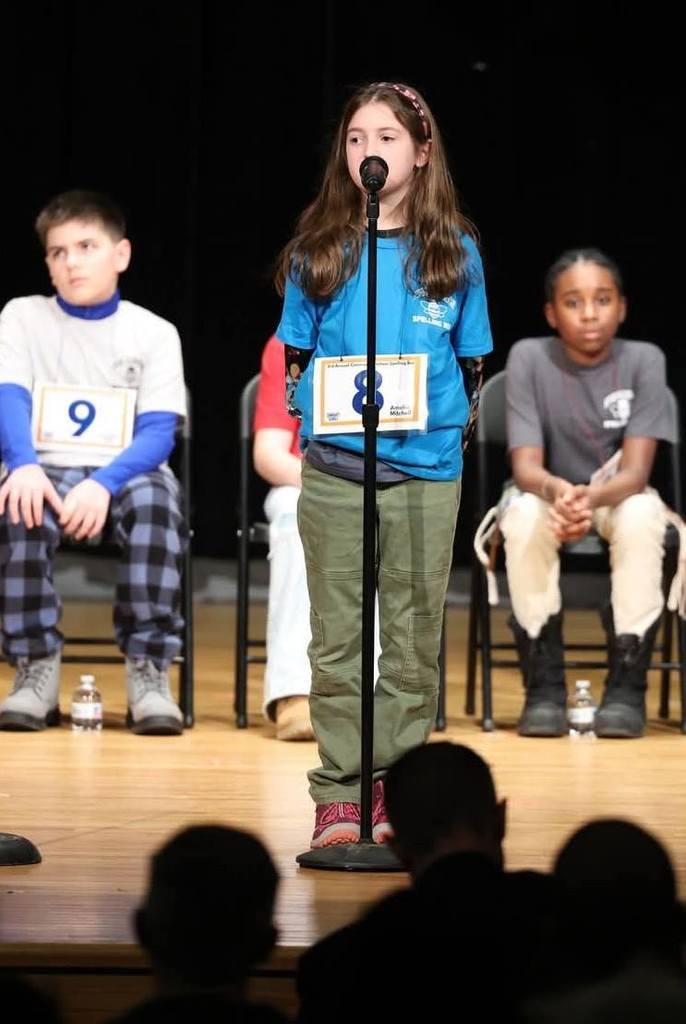 Young girl in a blue shirt speaking into a microphone.