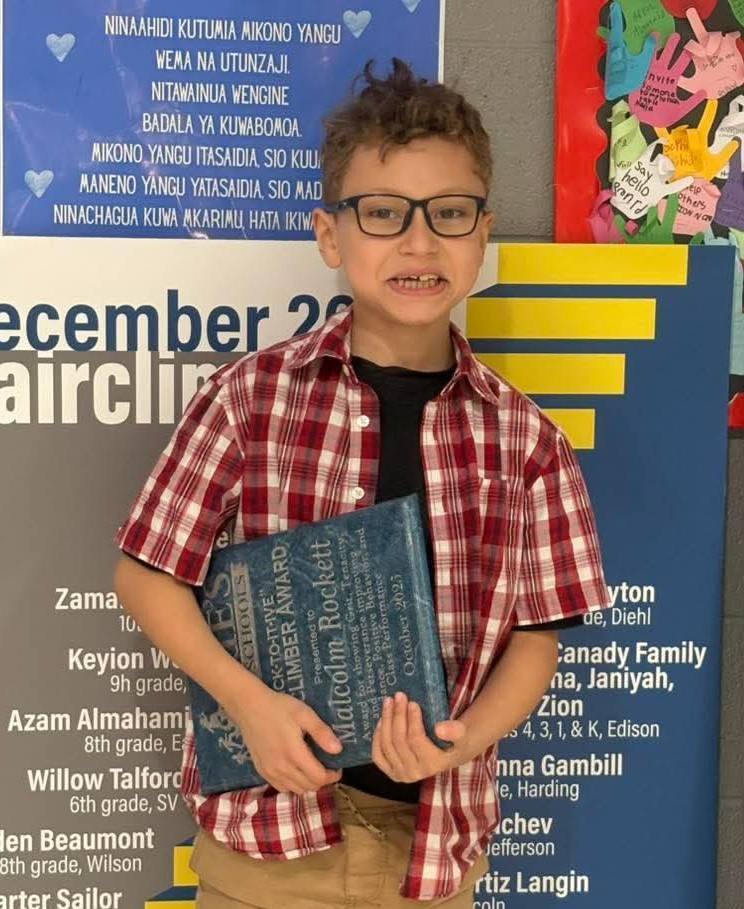 Young boy in a plaid shirt and is holding an award.
