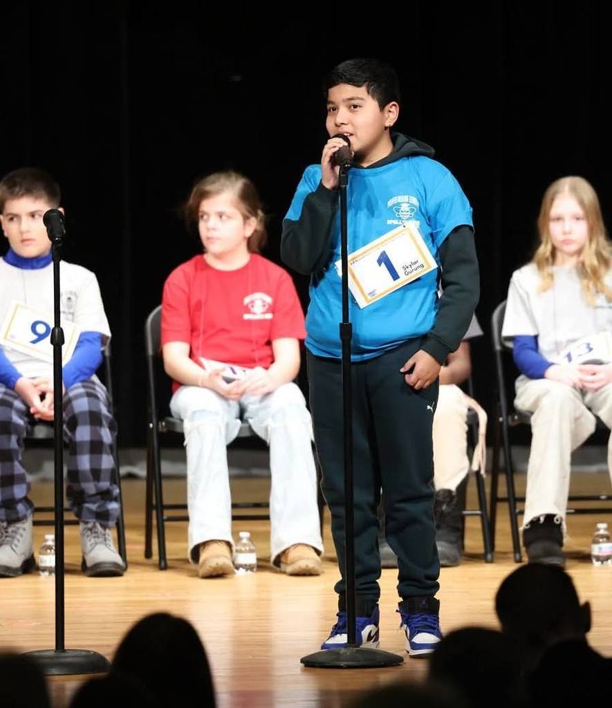 Young boy in a blue shirt speaking into a microphone.