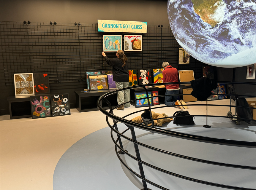 Art being put up on a black wall with an image of the world on the top right floating.