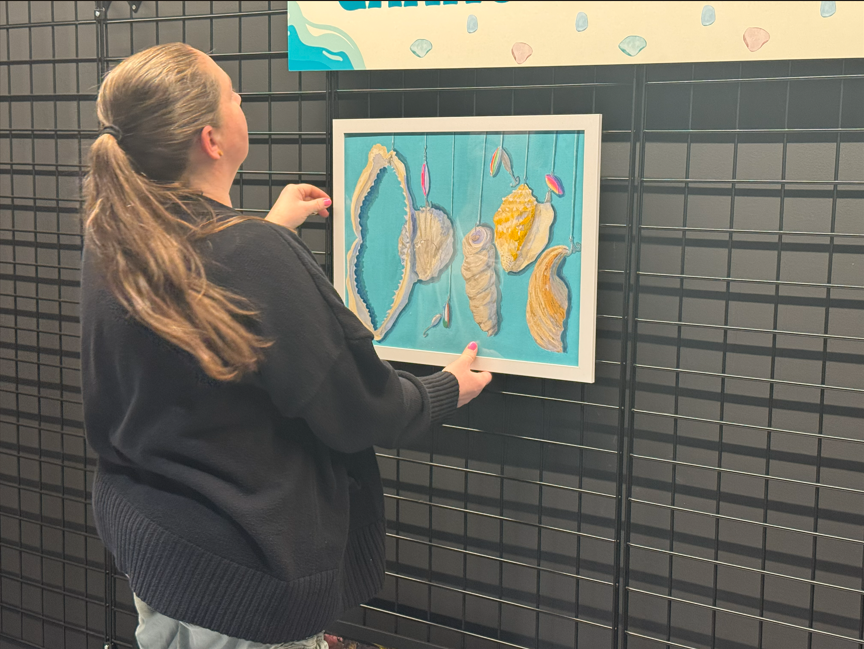 A women in a black sweater putting up artwork.