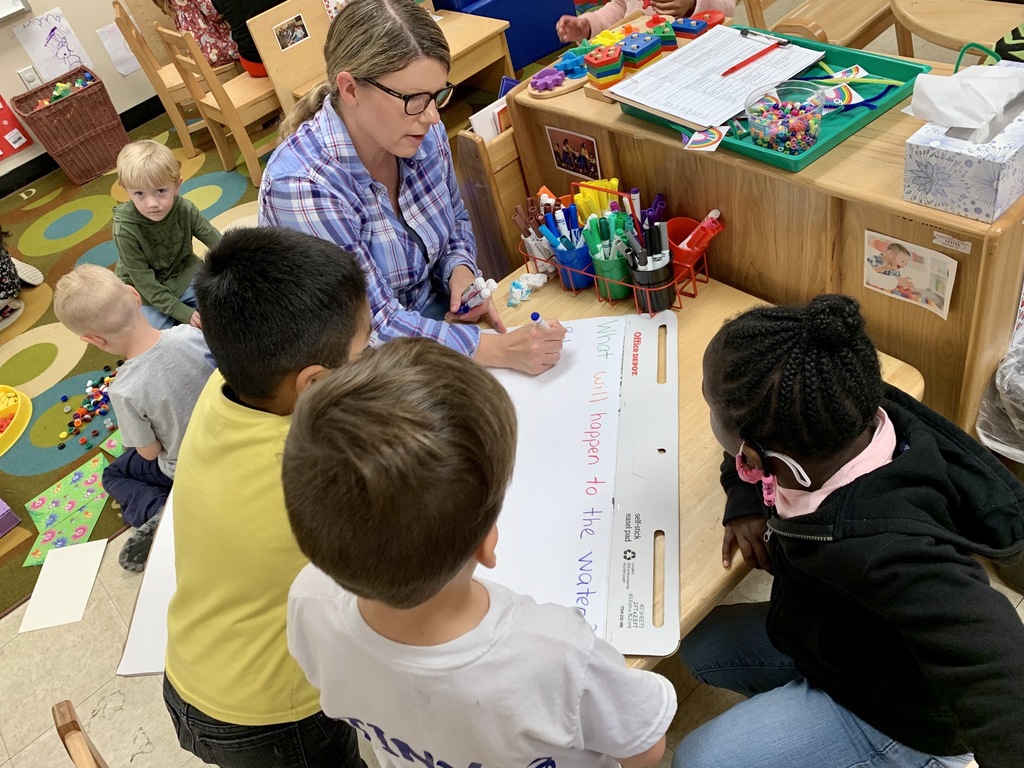 Mrs. Davis is writing down what three kids are telling her about what they think will happen with their science experiment.