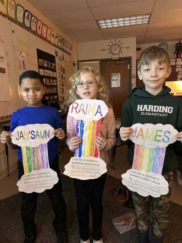 Students in a classroom holding up paper clouds with a colorful rainbow in between two clouds.