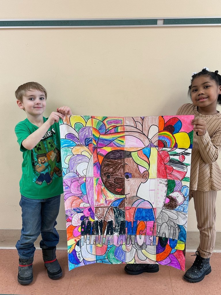 A young girl and boy standing in a hall and holding up colorful artwork.