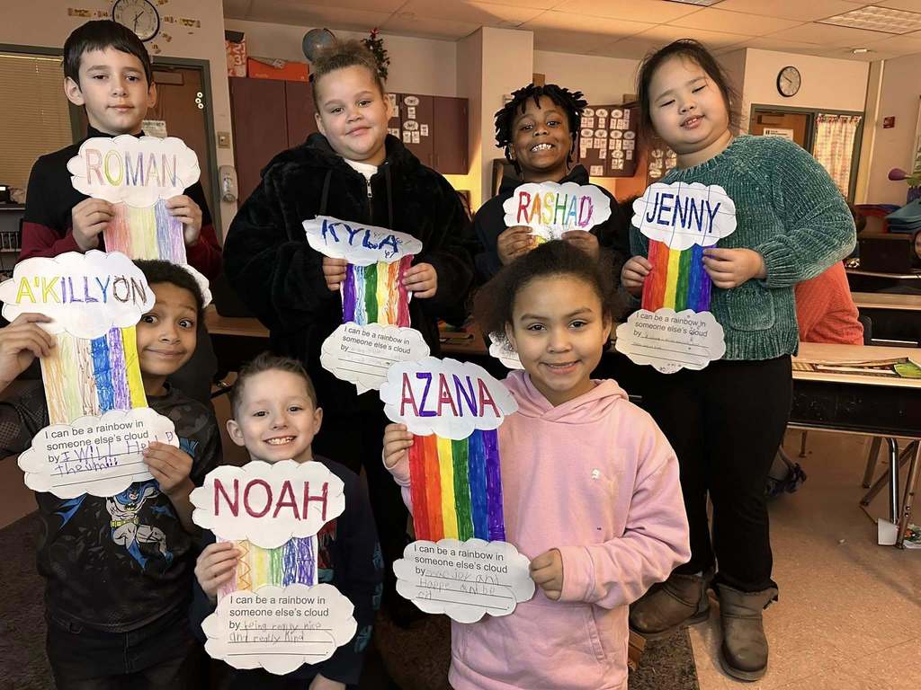 Students in a classroom holding up paper clouds with a colorful rainbow in between two clouds.