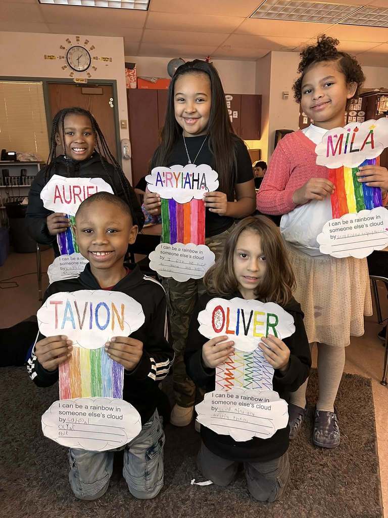 Students in a classroom holding up paper clouds with a colorful rainbow in between two clouds.