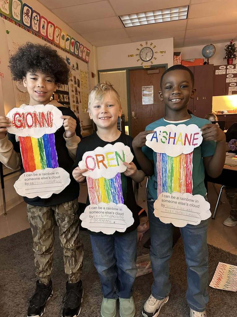 Students in a classroom holding up paper clouds with a colorful rainbow in between two clouds.