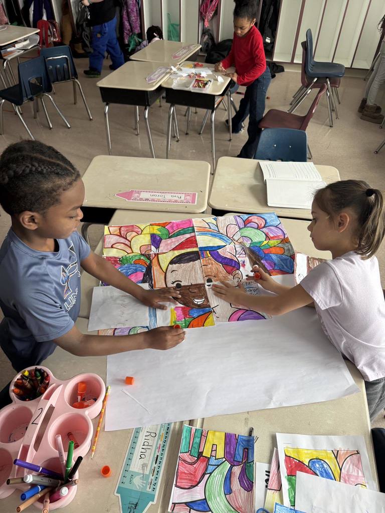 Kids at a desk coloring in a classroom.