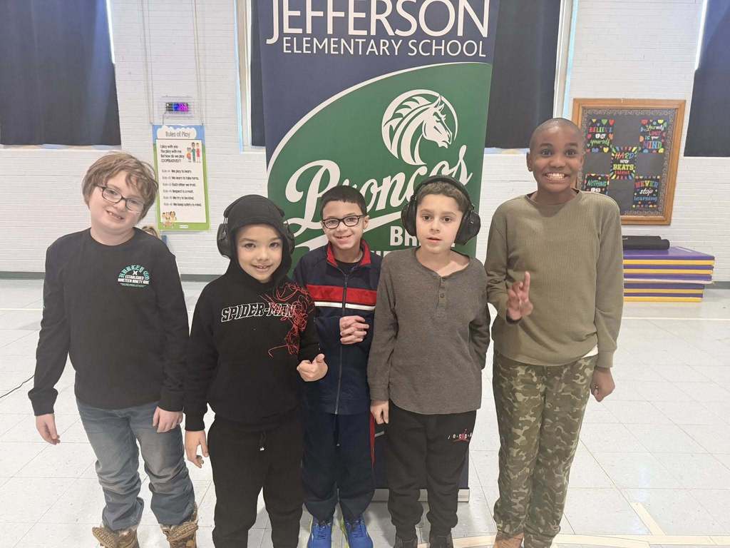 A group of students smiling in front of a green and blue sign, 