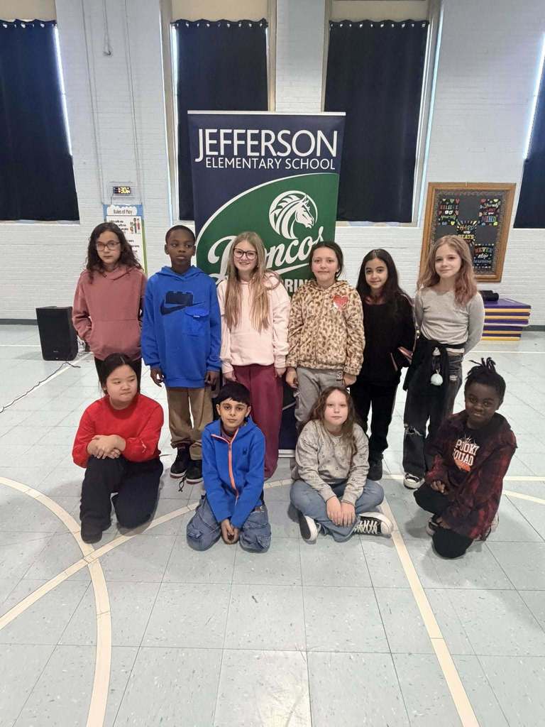 A group of students smiling in front of a green and blue sign, 