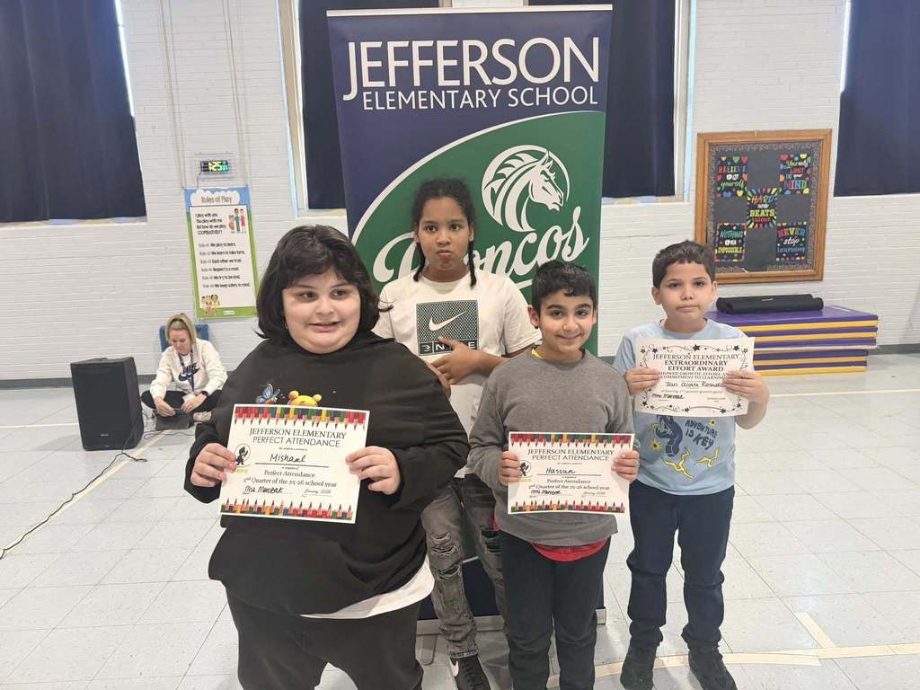 A group of students smiling in front of a green and blue sign, 