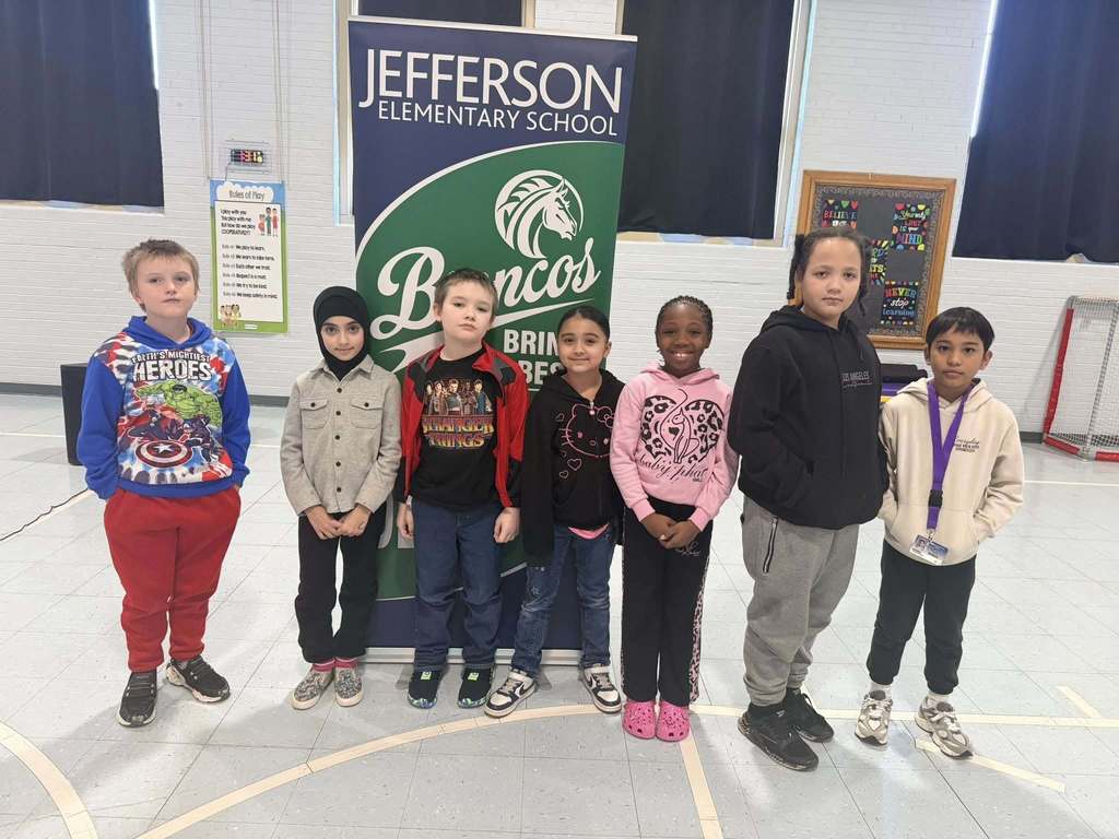 A group of students smiling in front of a green and blue sign, 