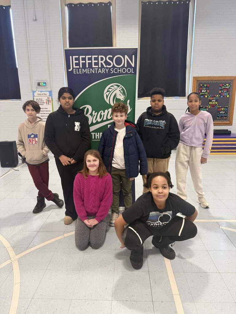 A group of students smiling in front of a green and blue sign, 