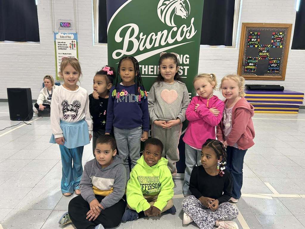 A group of students smiling in front of a green and blue sign, 