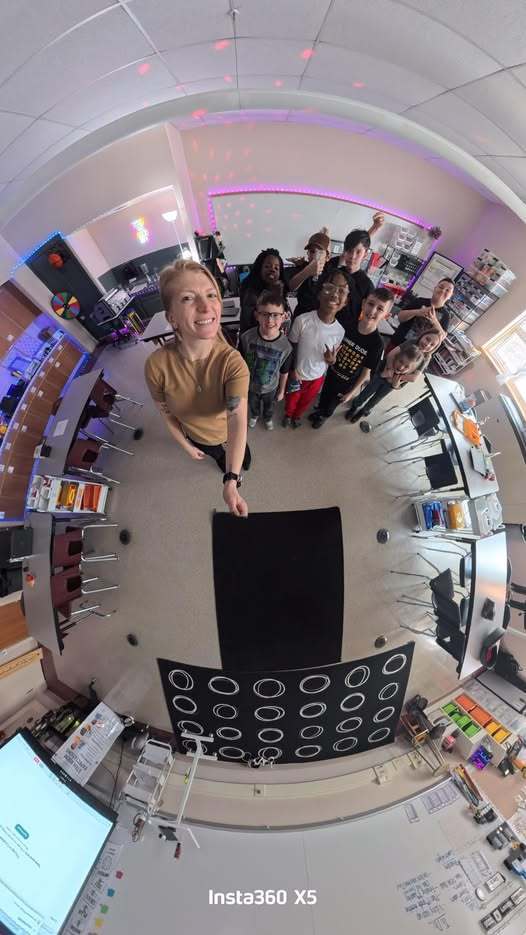 A female adult taking a photo with her students in a classroom.