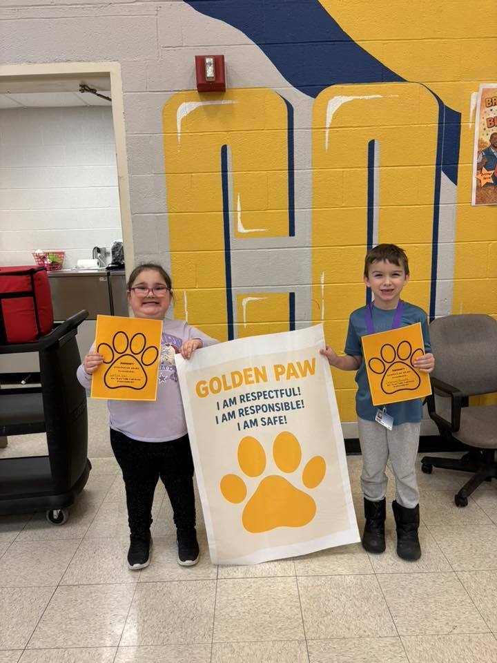 A young girl and boy holding up paper and yellow paw prints.