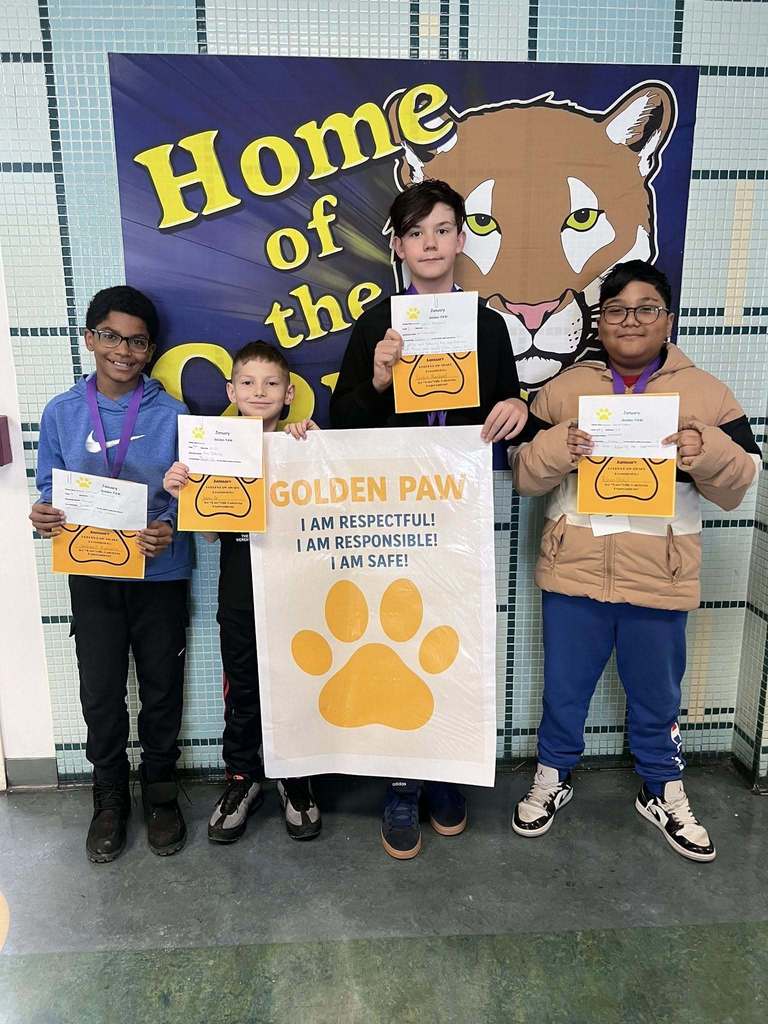 A group of students in a hall holding up paper and yellow paw prints.