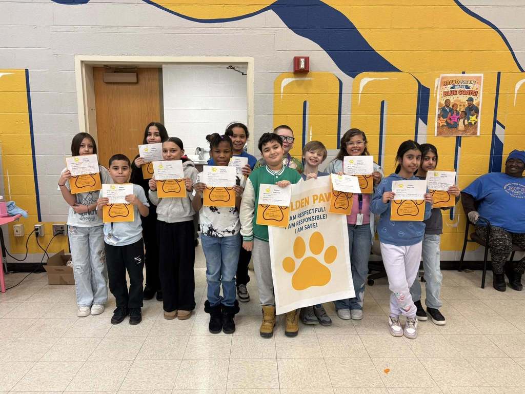 A group of students in a hall holding up paper and yellow paw prints.