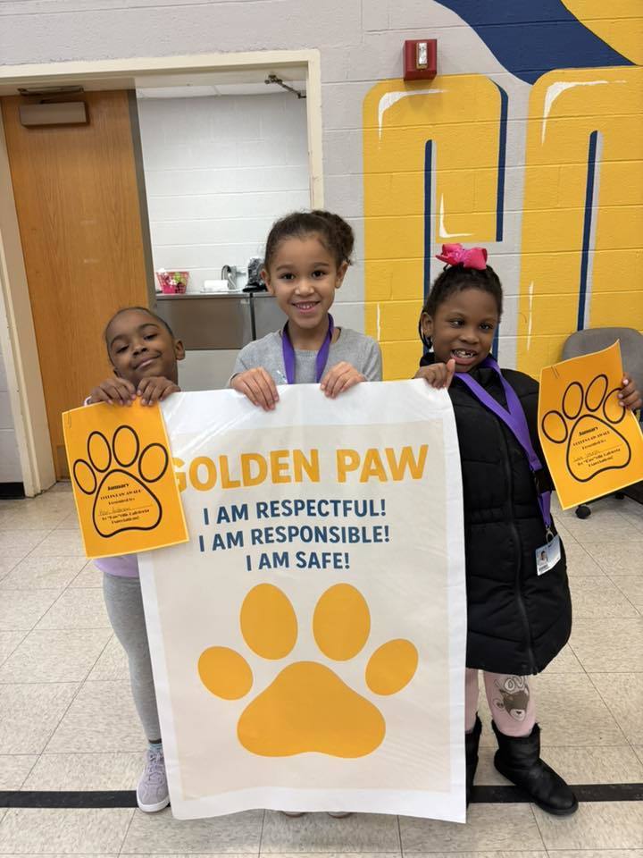 Three young girls holding up paper and yellow paw prints.