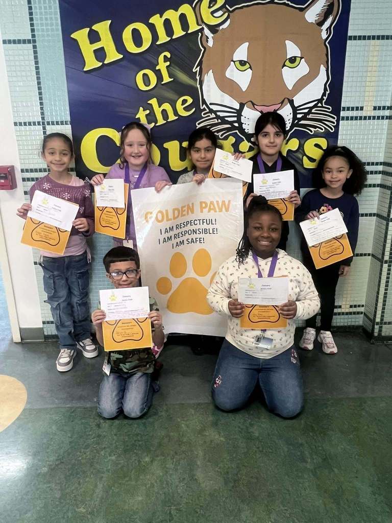 A group of students in a hall holding up paper and yellow paw prints.