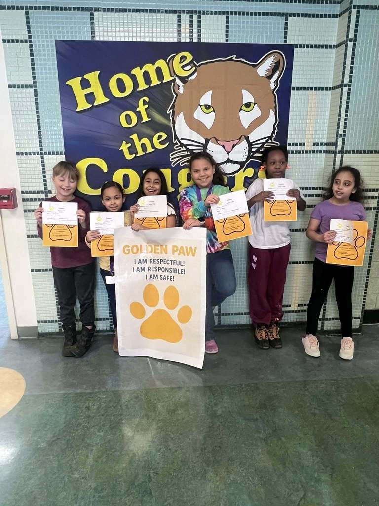 A group of students in a hall holding up paper and yellow paw prints.