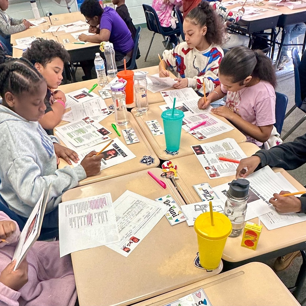 Kids sitting at tables in a classroom and working while they all have colorfult water bottles on their desks. 