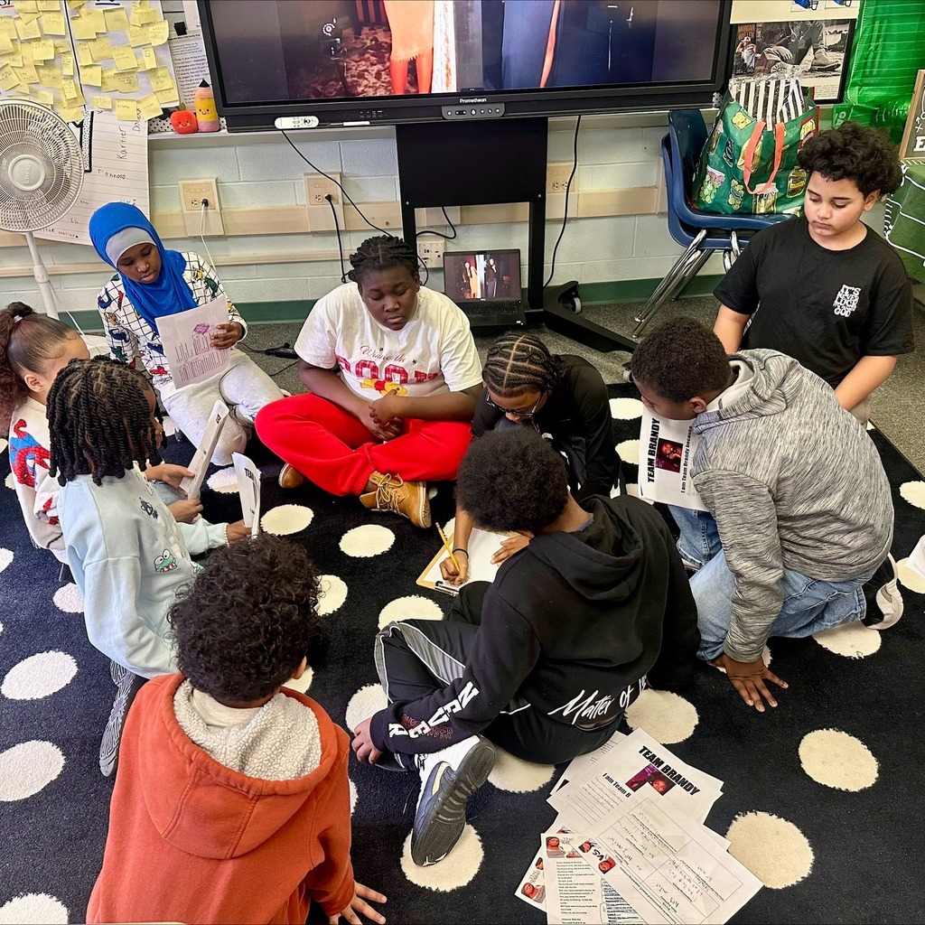 A group of students working on a polka dot rug in a classroom. 
