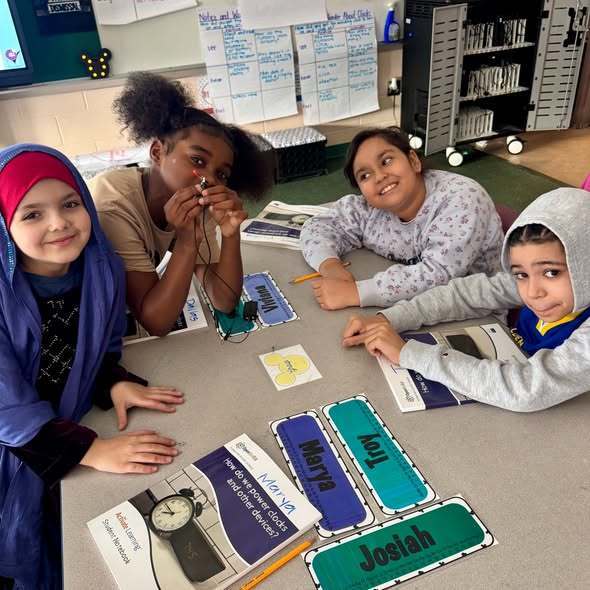 Students in a classroom sitting at a desk smiling. 