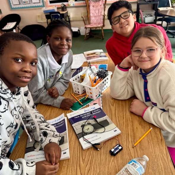 Students in a classroom sitting at a desk smiling. 