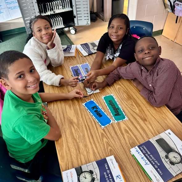 Students in a classroom sitting at a desk smiling. 