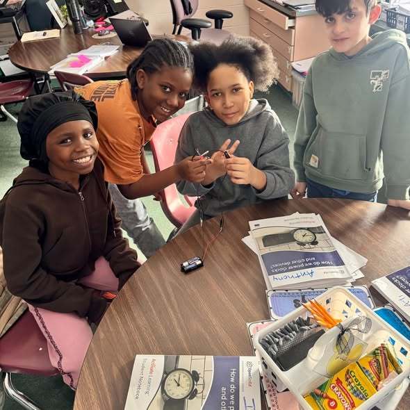 Students in a classroom sitting at a desk smiling. 