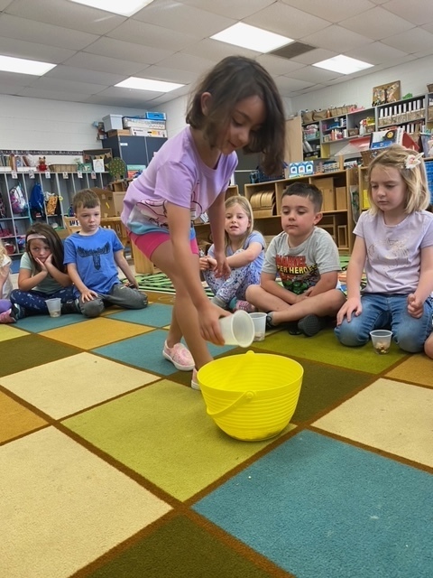 A little girl is adding a cup of food to the class trail mix.