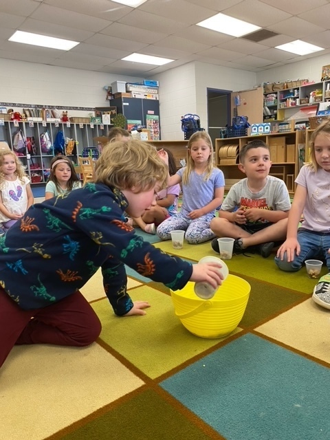 A little boy is pouring food into a bowl to make a class trail mix.