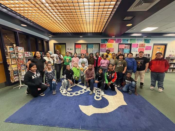 A group of students in a library while standing on a blue and green carpet. 