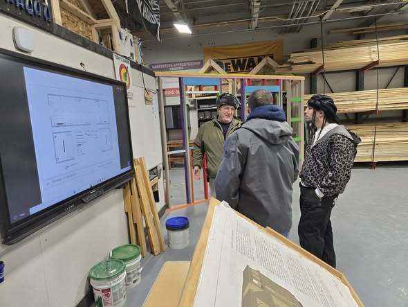 Three individuals talking and there is a television on the wall with an outline.