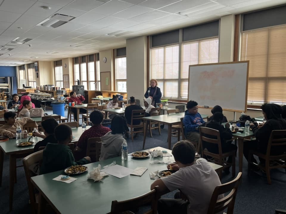 Kids sitting in a classroom while an adult talks. 