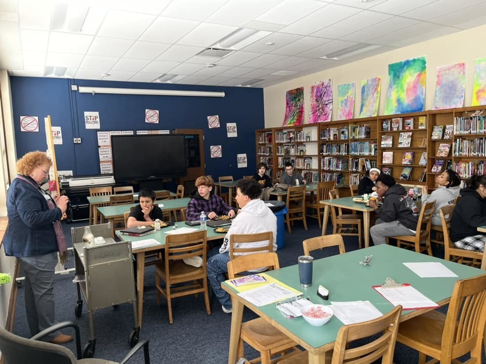Kids sitting in a classroom while an adult talks. 