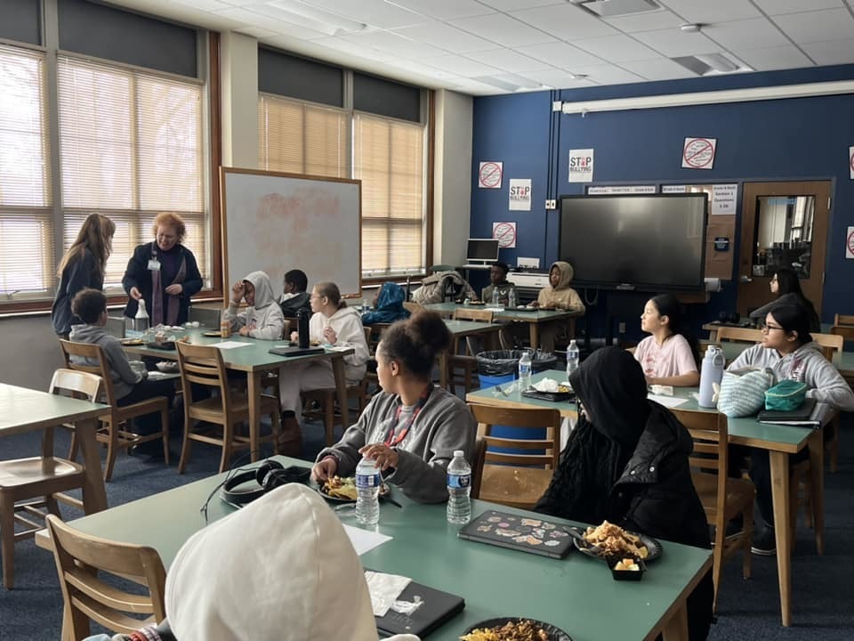 Kids sitting in a classroom while an adult talks. 