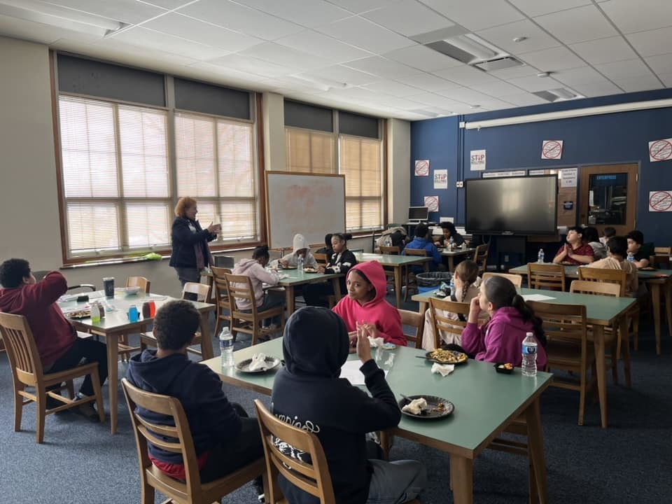 Kids sitting in a classroom while an adult talks. 