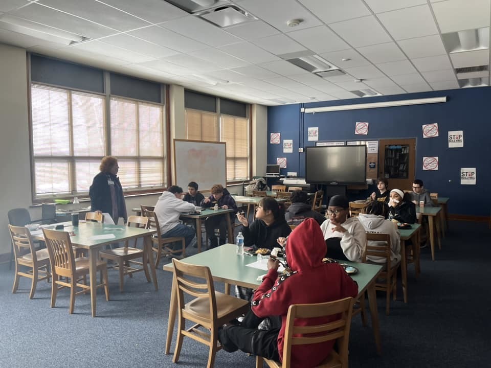 Kids sitting in a classroom while an adult talks. 